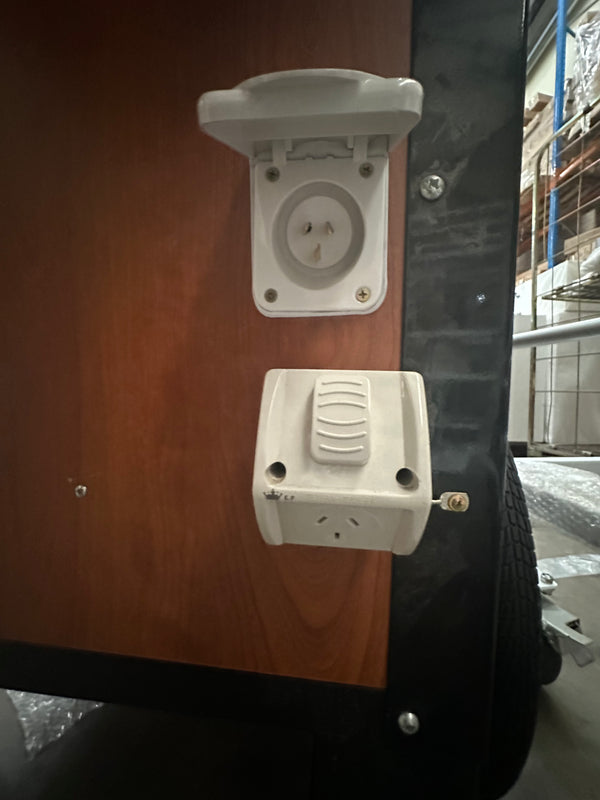 Close-up view of power outlets on a mobile serving cart from PromoWheels, featuring an electrical socket and a switch, designed for Coffee, Food & Charcuterie Carts for Events, Catering & Business.