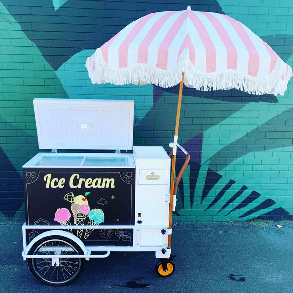 Ice cream cart with a pink and white striped umbrella, featuring 'Ice Cream' branding, available from PromoWheels, perfect for events and mobile food businesses.